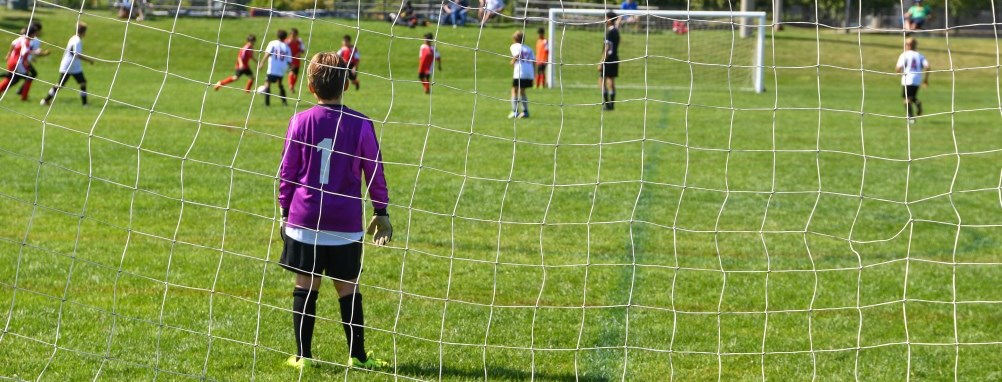 A goalie on the soccer field minding the net at a soccer game