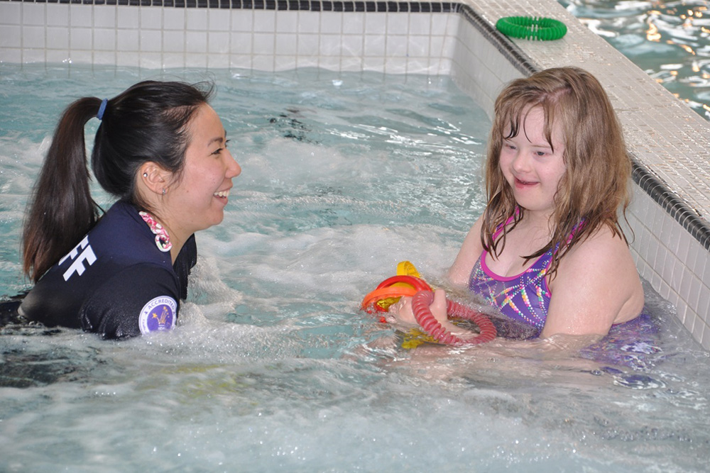 An inclusion camp counselor playing in the pool with a little girl