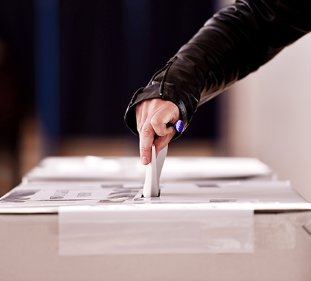 A hand dropping a ballot into a box on a table